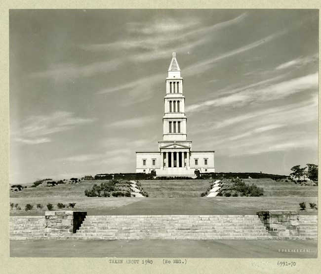 Large white building with a point on a hill, with terraced grass