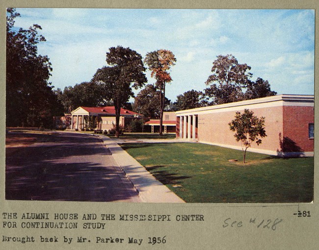 Image of low campus buildings on grassy area with few trees around.