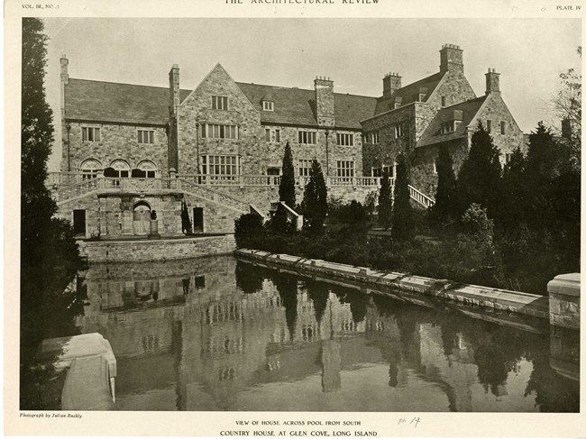 Black and white of large stone home like castle with rectangular pool in background with trees planted on the edges.