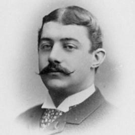 Black and white photograph of elderly man with thick dark head of hair and a dark handlebar mustache wearing a suit and tie