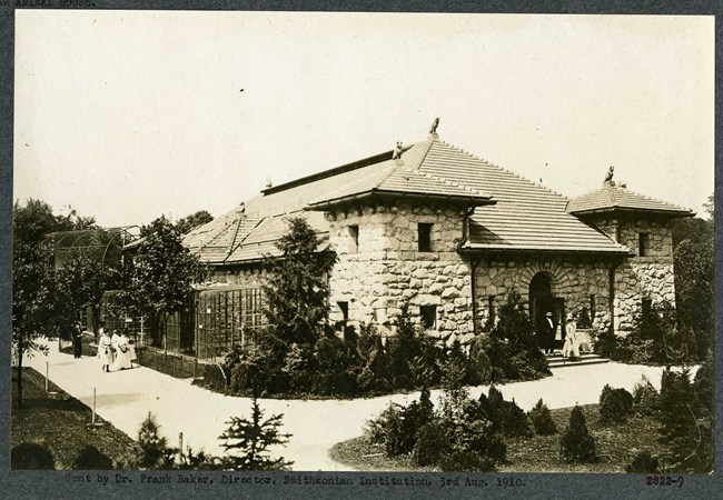 Black and white of stone building surrounded by plants and a path