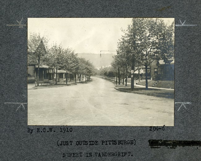 Black and white of curving road going through community with houses and trees on both sides.