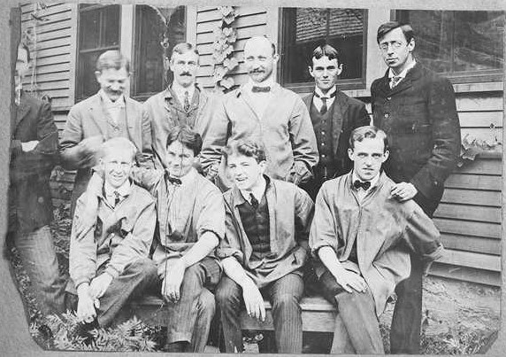 Black and white of men in suit posed for picture in front of home