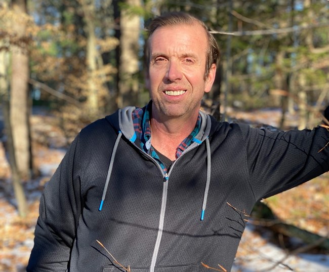 Man poses for picture in woods, smiling.