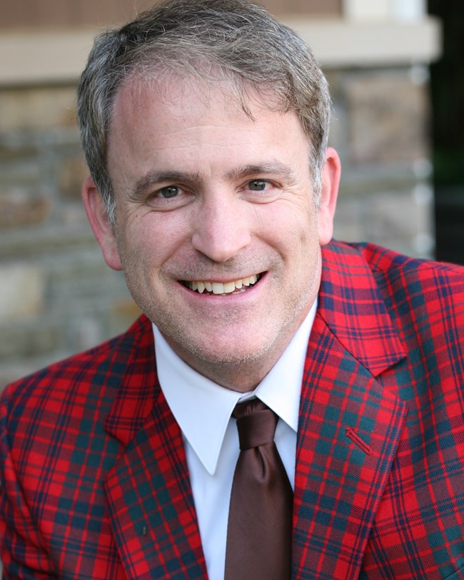 Man wears red plaid jacket with a brown tie.