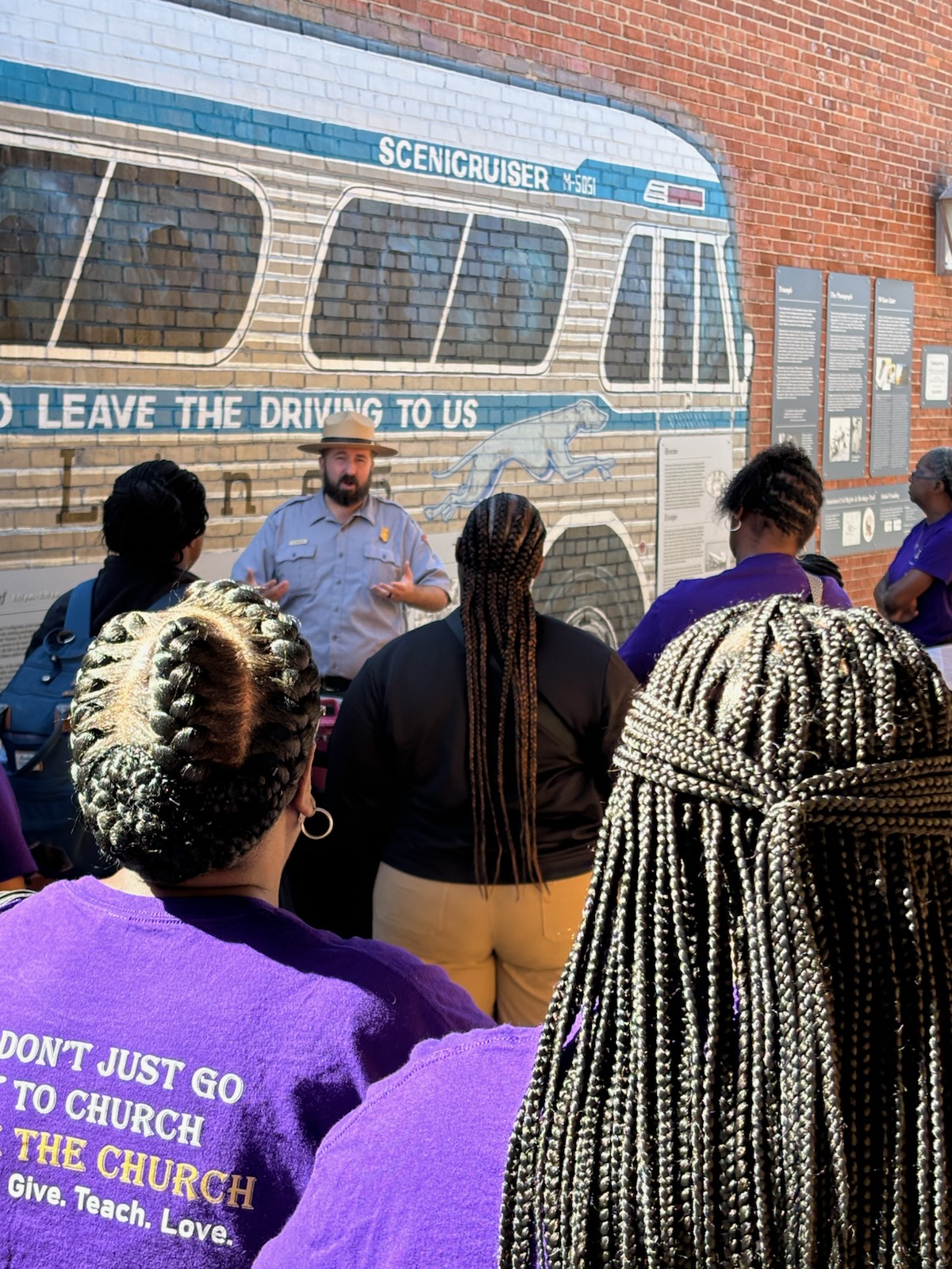 A ranger stands in front of a bus mural talking to a group of visitors.