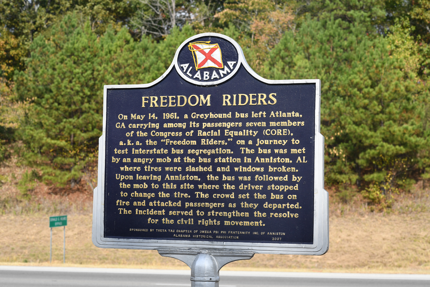 Historical marker near bus burning site, 2016, DOI Photo A black metal sign with yellow text tells the story of the freedom riders attacked at this location in 1961.