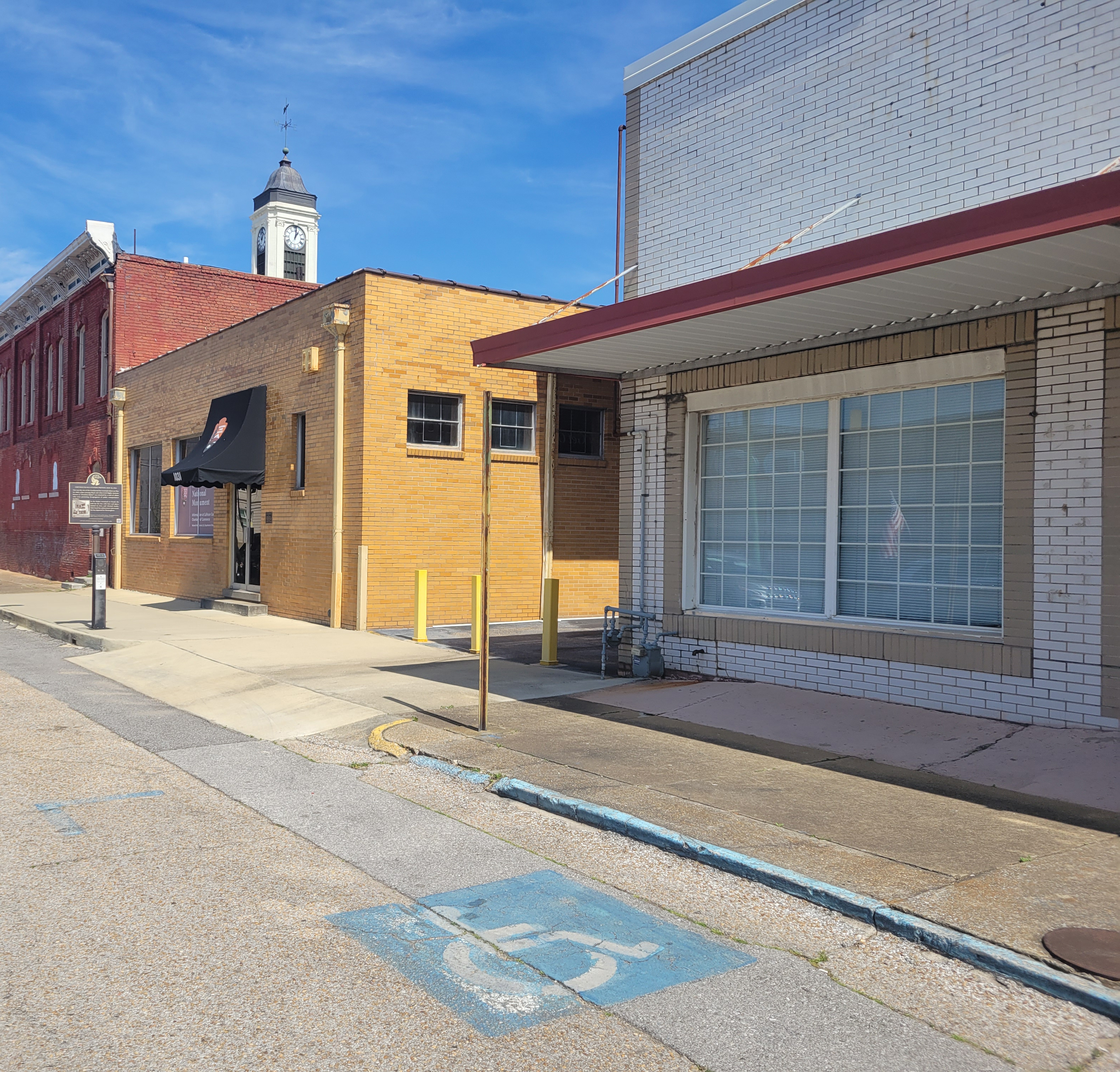 A brick building with an ADA parking spot in front. Two more brick buildings are down the street.