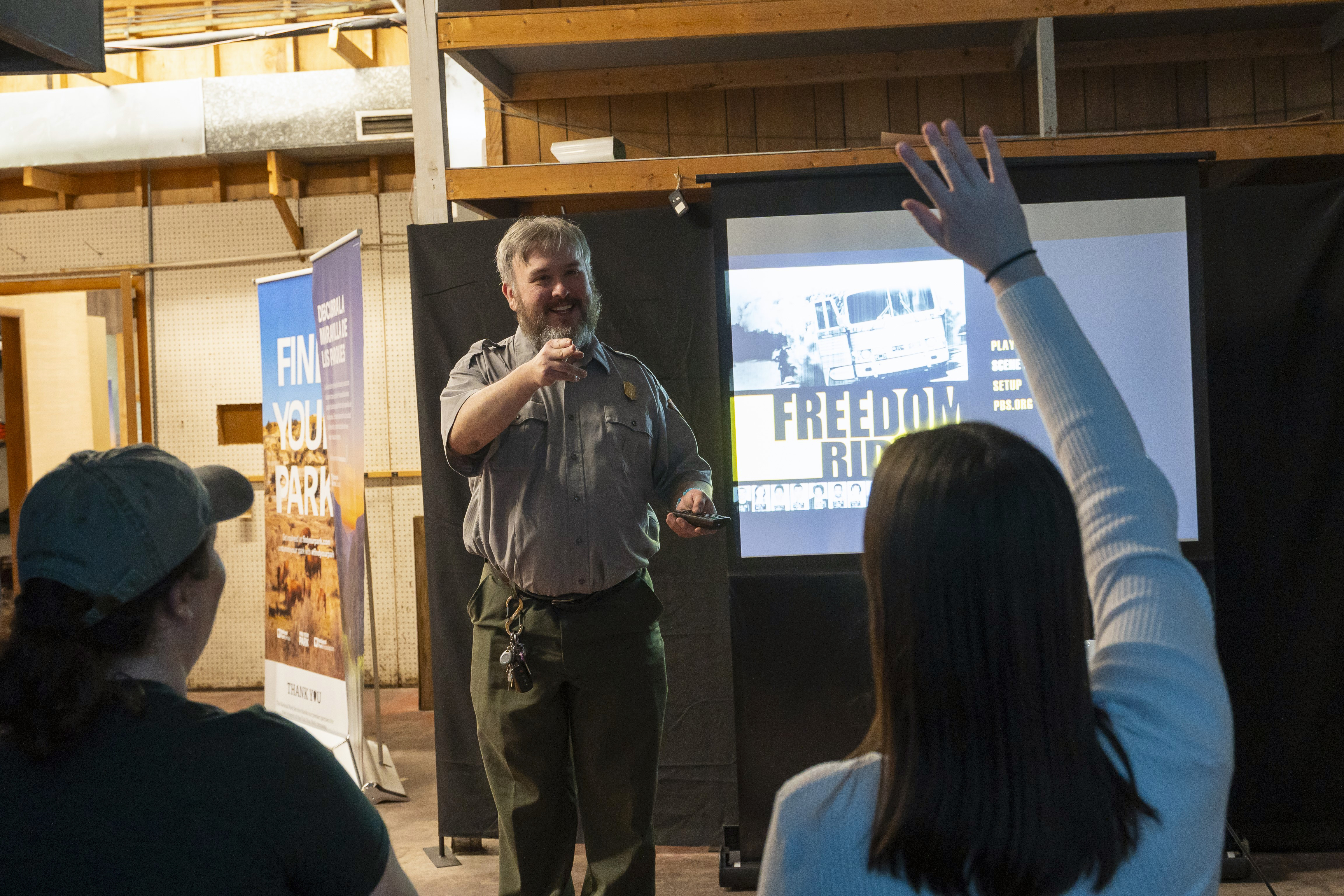 A ranger answering questions from visitors in front of a screen before the showing of a park film.