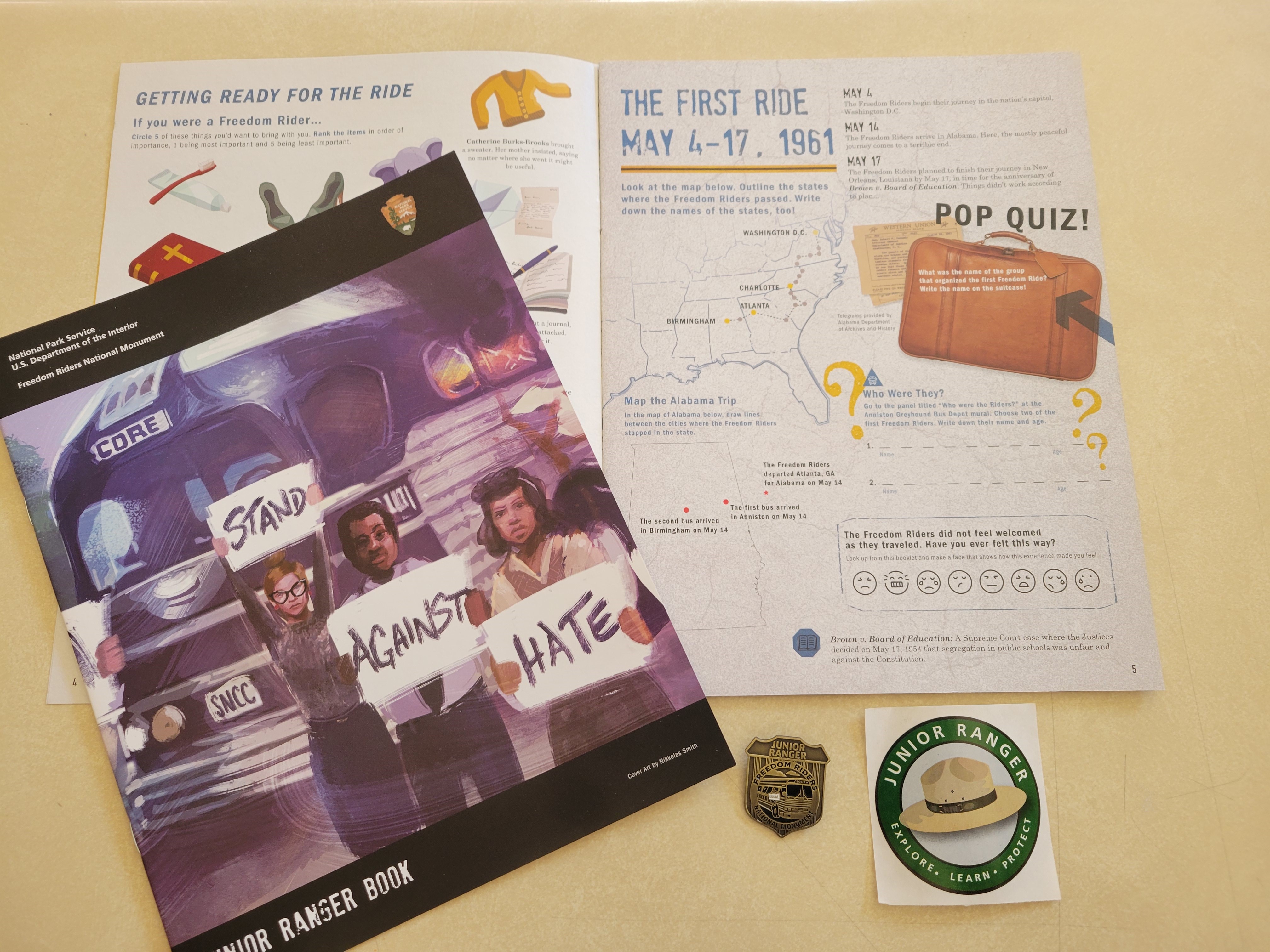 A Junior Ranger book lays open on a desk with another closed on top of the open book. Below the open book is a Junior Ranger Badge and sticker