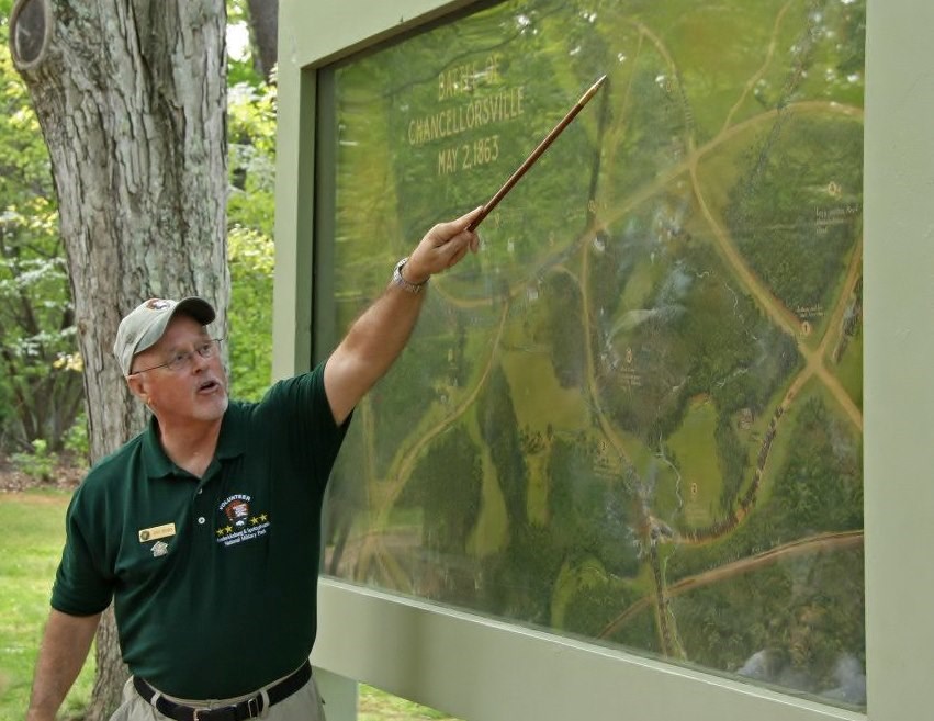 Volunteer leading a guided walking tour at Chancellorsville by pointing out features on a large battle painting Volunteer leading a guided walking tour at Chancellorsville by pointing out features on a large battle painting