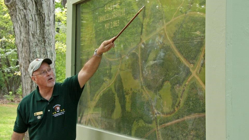 A park volunteer conducts a walking tour A volunteer in a green polo pointing at a large battle painting