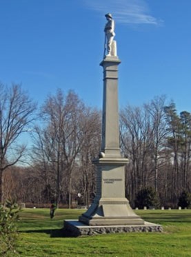 Tall monument in center of Spotsylvania Confederate Cemetery with grass and trees
