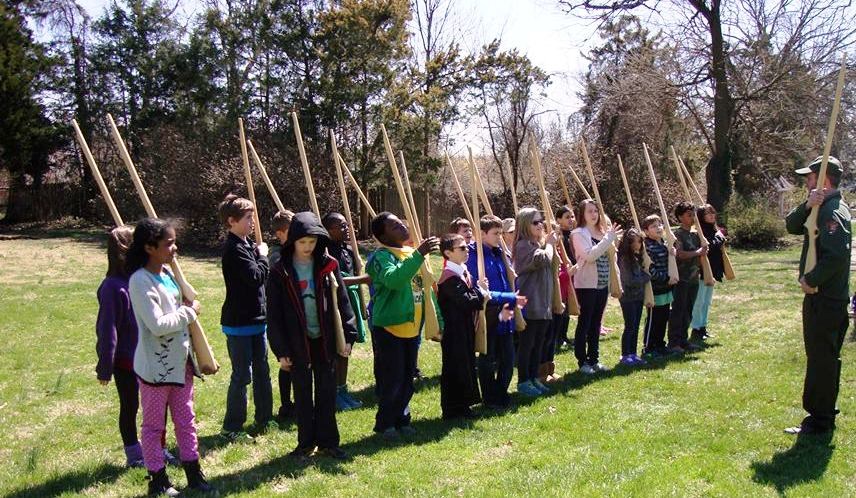 Park ranger faces line of children, all holding wooden rifles Park ranger faces line of children, all holding wooden rifles