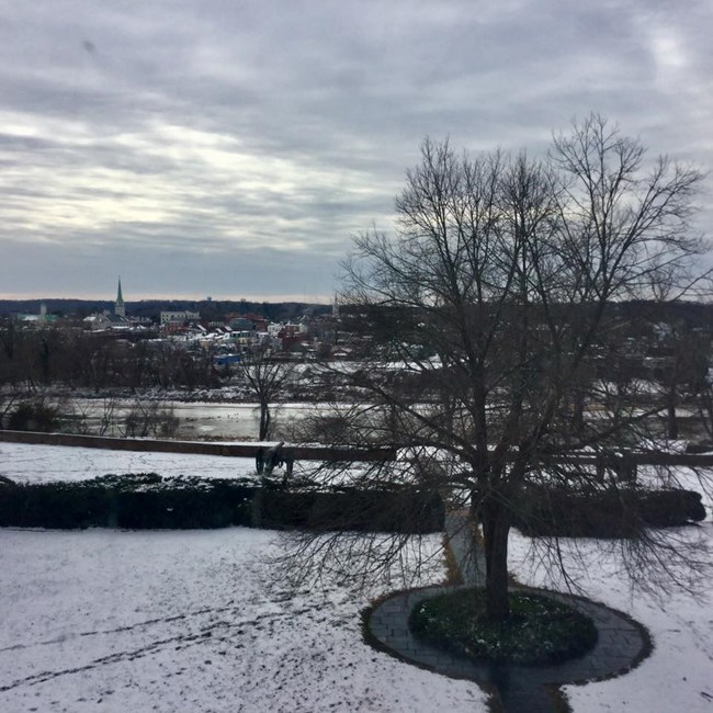 View overlooking terraces down to the river, with the town of Fredericksburg in the background - the ground is covered in snow and there is ice in the river