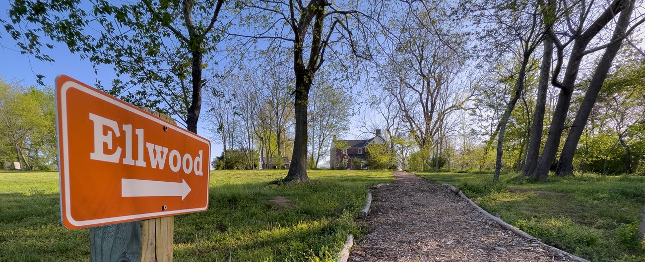 A sign that says Ellwood pointed along a path leading to a two story red house.