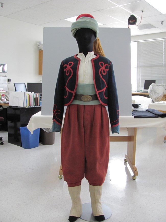 Zouave uniform consisting of blue coat with red piping, red pants, and fez displayed on mannequin