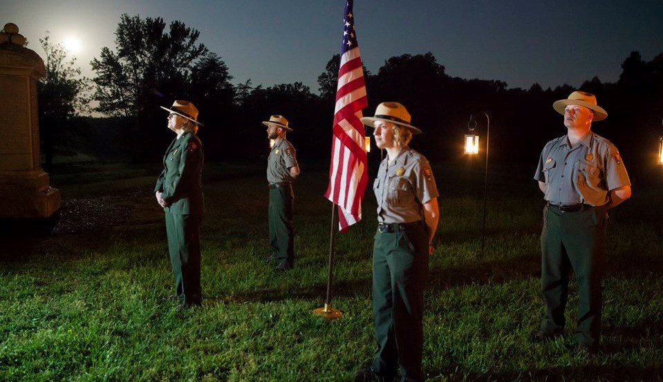 Four park historians stand as silent sentinels around an American flag at the Bloody Angle at night with the moon overhead Four park historians stand as silent sentinels around an American flag at the Bloody Angle at night with the moon overhead