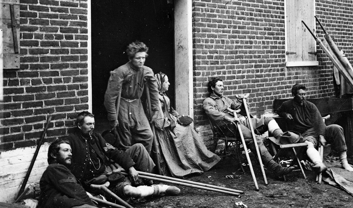 Wounded soldiers resting outside the Sanitary Commission depot in Fredericksburg, 1864. One woman is seated in doorway Wounded soldiers resting outside the Sanitary Commission depot in Fredericksburg, 1864. One woman is seated in doorway