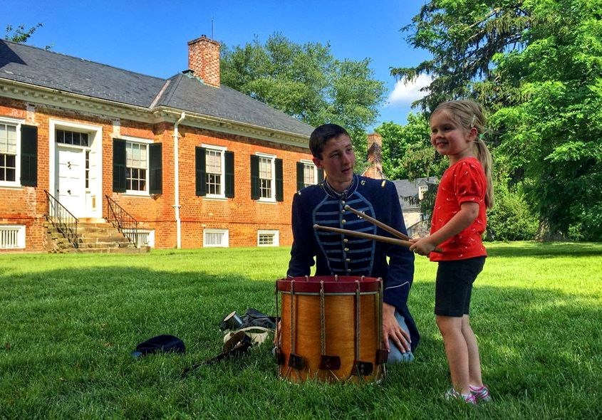 Child plays drum during living history event under supervision of Union drummer with Chatham Manor in background Child plays drum during living history event under supervision of Union drummer with Chatham Manor in background