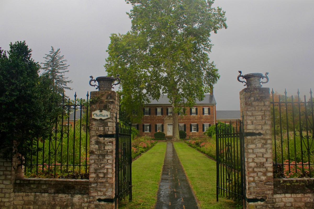 Large brick Georgian-style house and garden with stormy sky in background Large brick Georgian-style house and garden with stormy sky in background