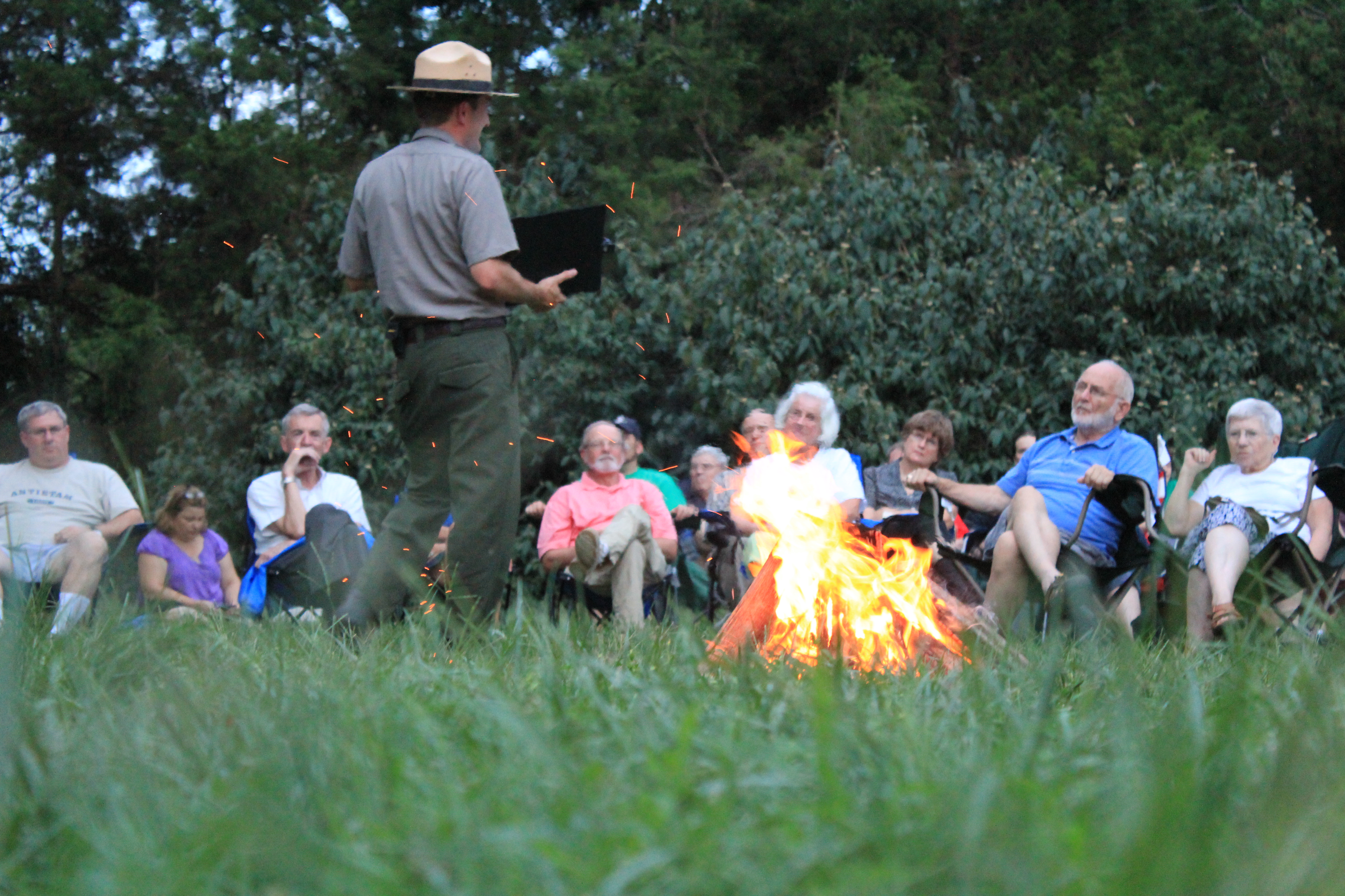 Ranger talks next to a blazing campfire with audience in the background