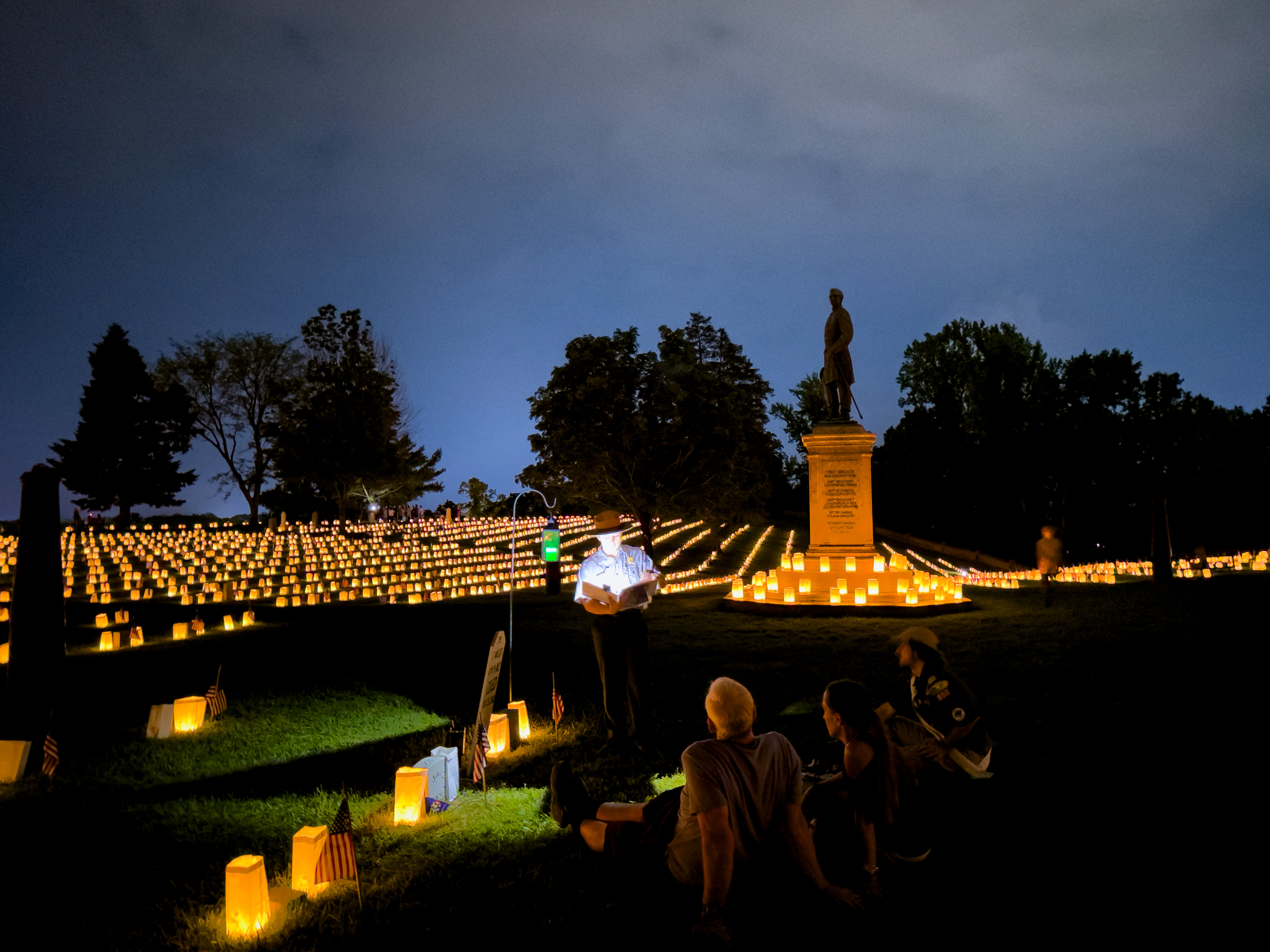 Ranger speaking in a cemetery lit by luminarias