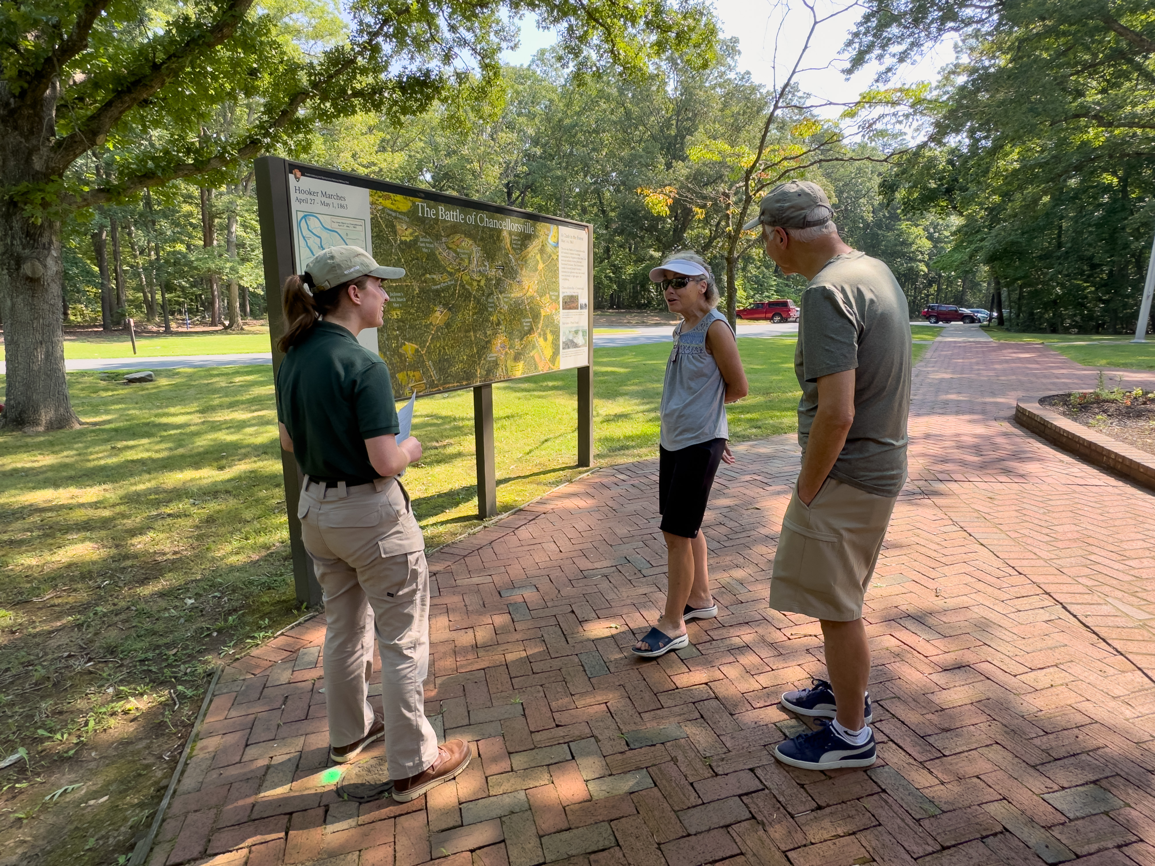 Summer 2024 at Chancellorsville A park volunteer talks to two people at a large battle illustration.