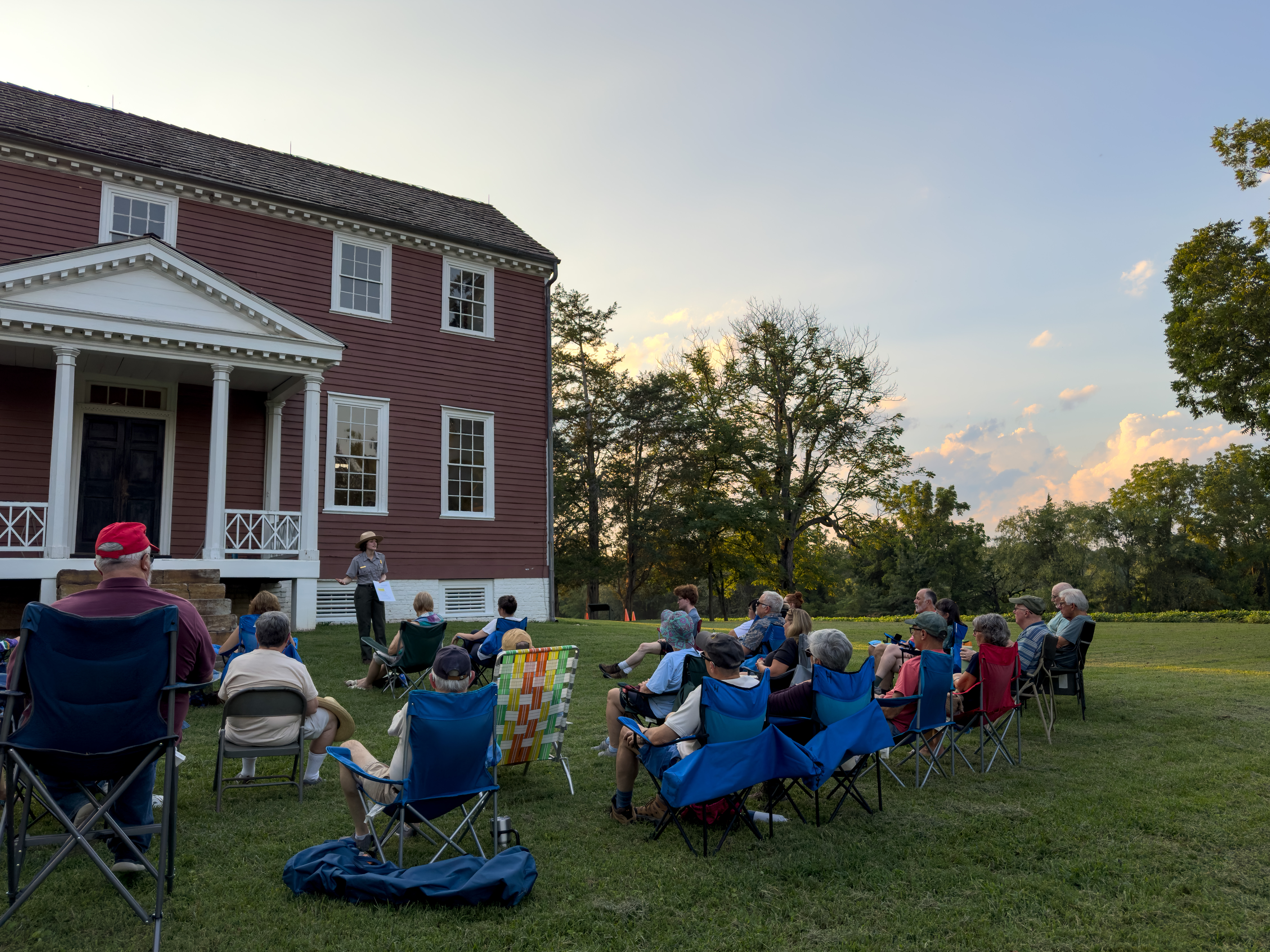 2024 Ellwood History at Sunset A ranger speaks to a crowd on a lawn outside a historic house.