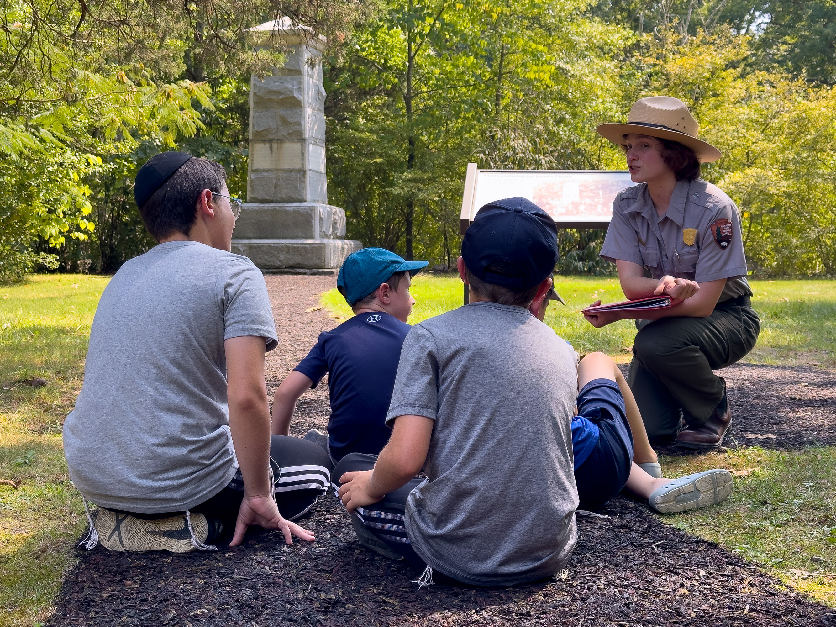 A park ranger speaks to three children in front of a monument on a battlefield.