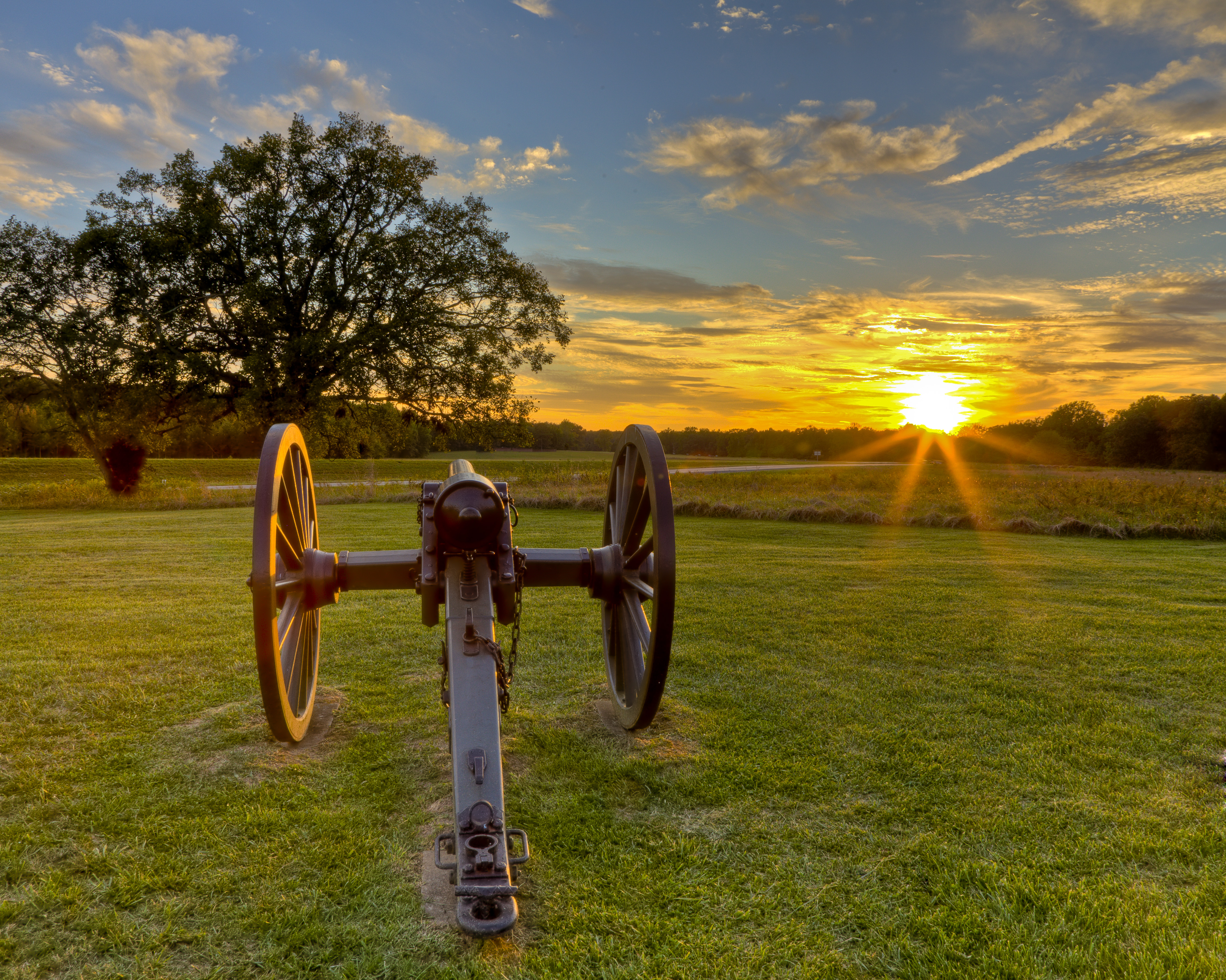 Cannon in front of fields with distant tree line and sun setting in background