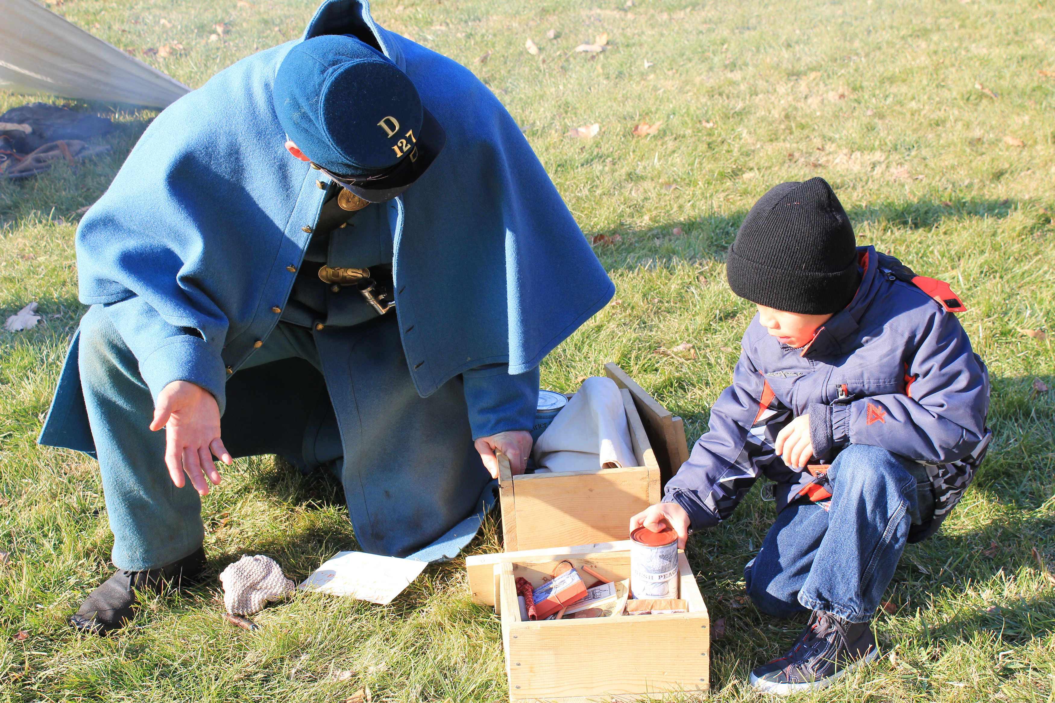 Chatham Living History A living historian dressed as a United States soldier in the Civil War looks at a box of period food with a small boy.