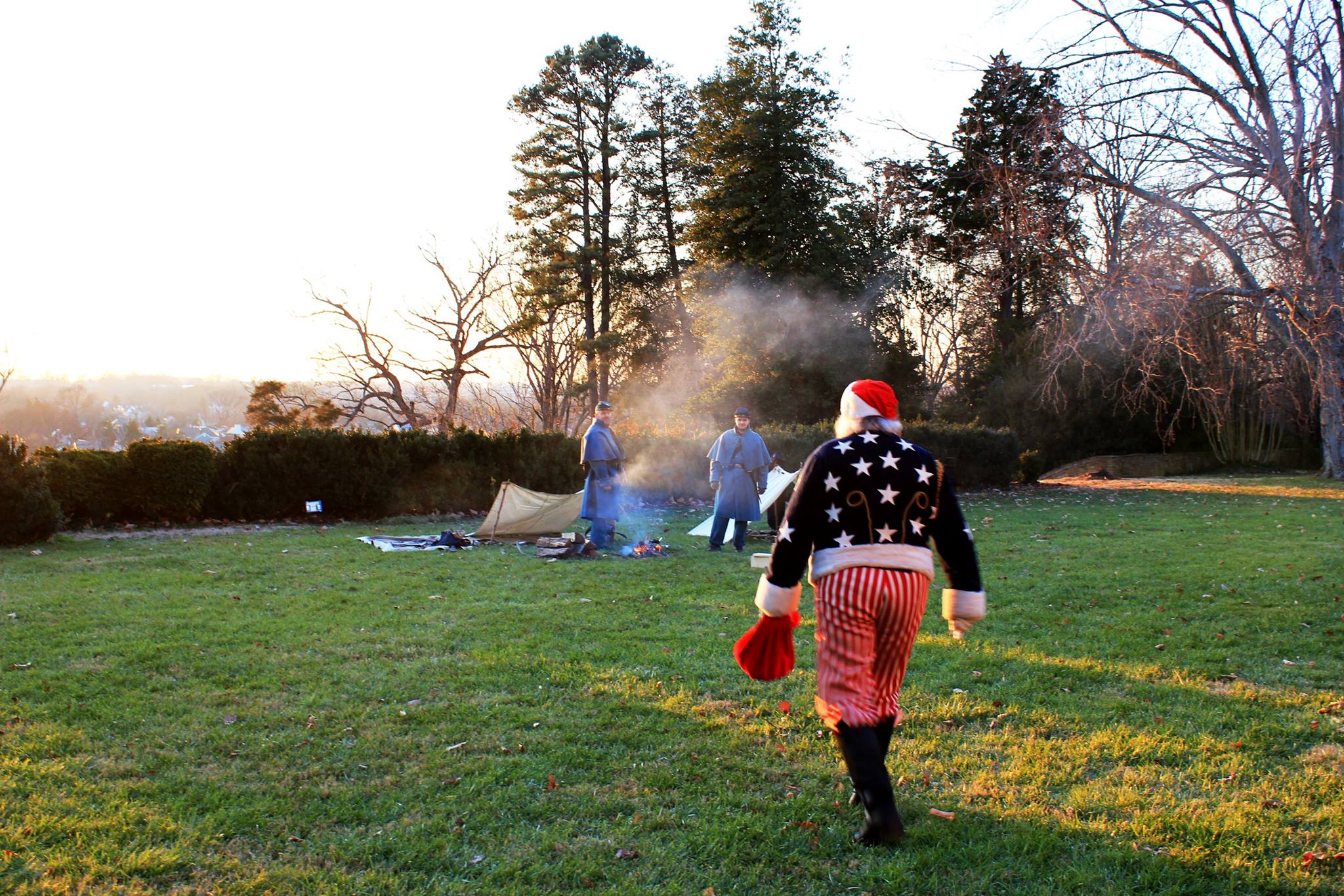 Santa in red, white and blue Civil War era costume walks toward Union soldiers at campfire.