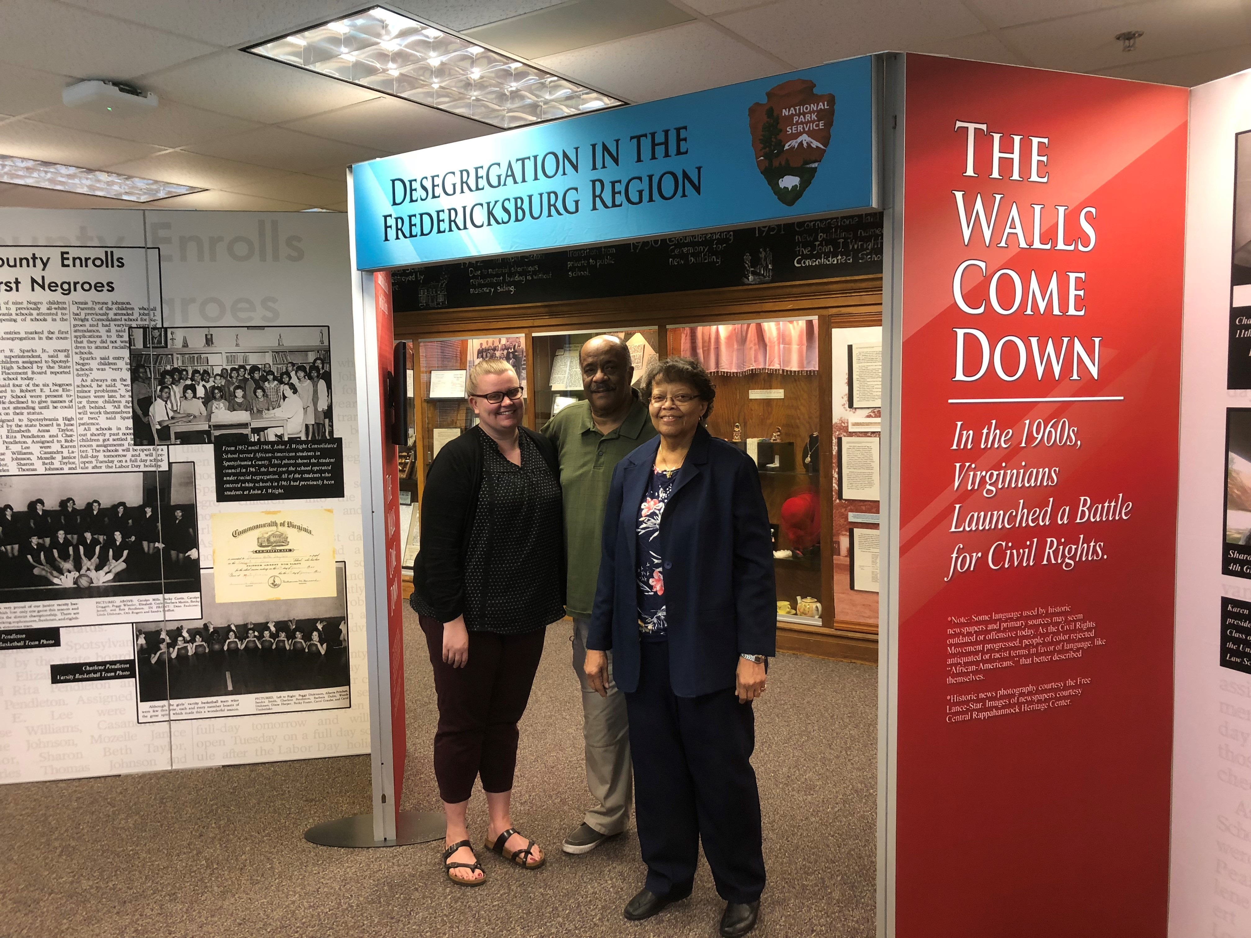 Three people stand in the center of a colorful exhibit on desegregation