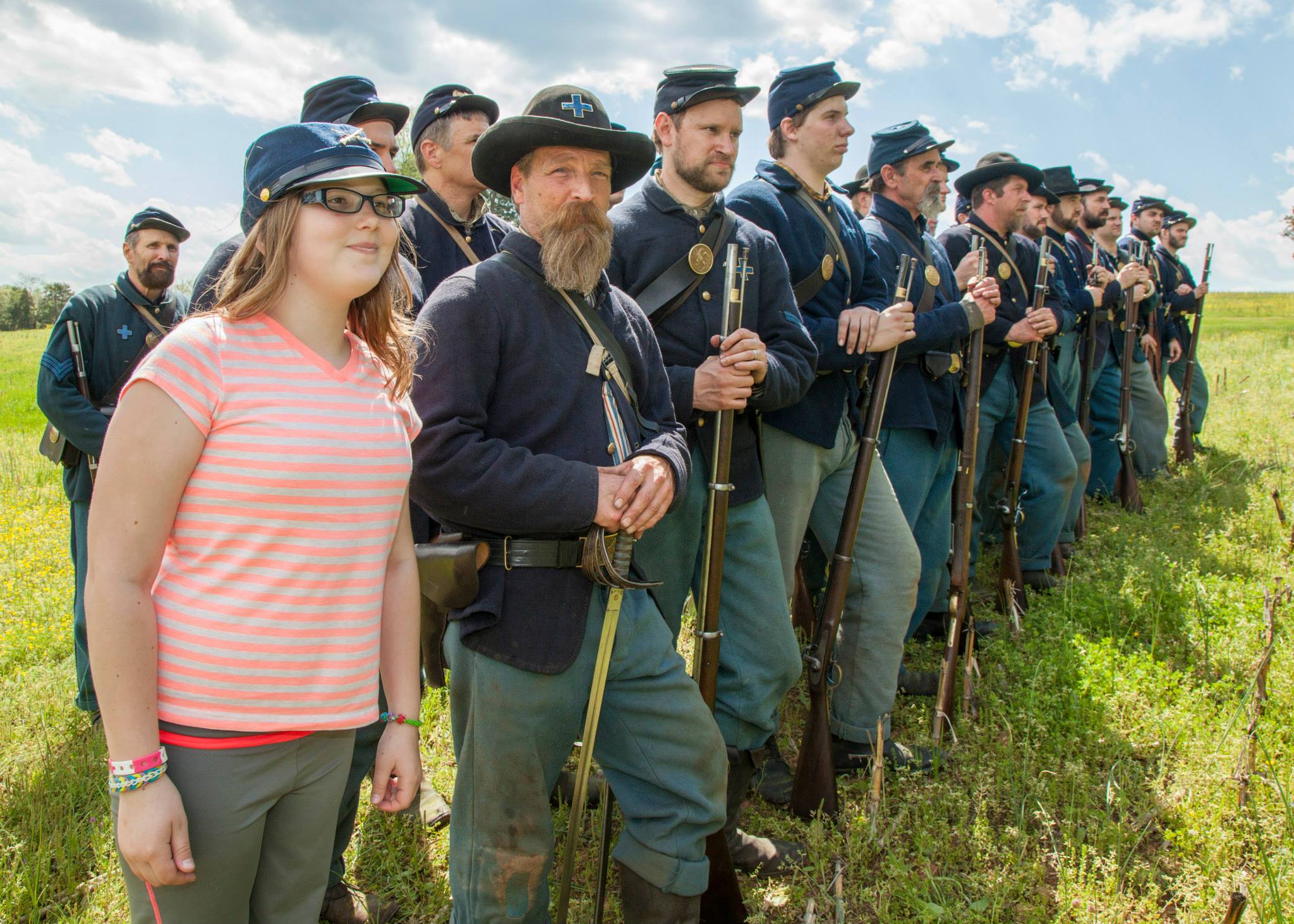 A girl wearing a soldier's hat stands with a row of reenactors