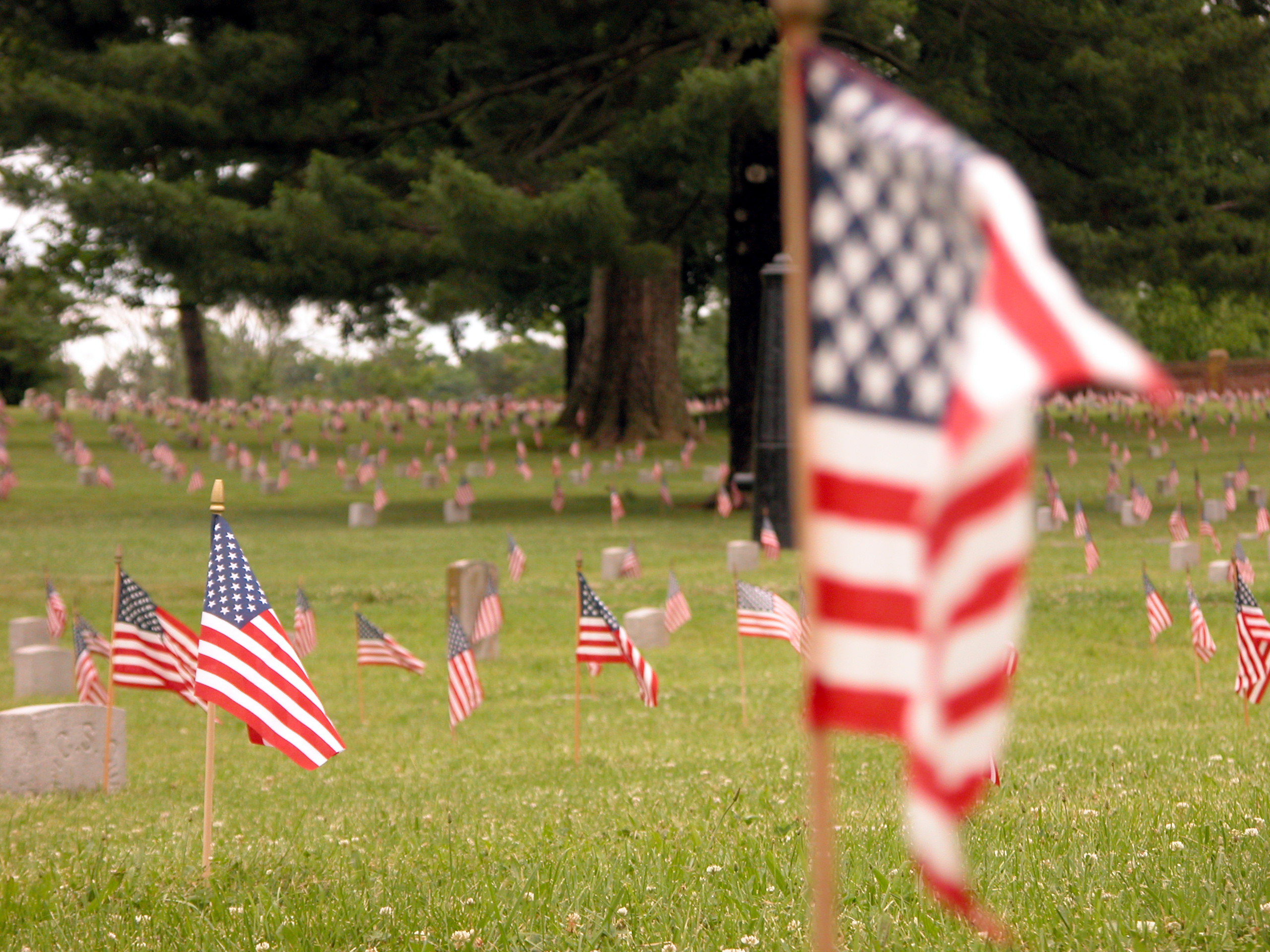 American flag waving in wind in foreground with soldier graves decorated by American flags in background