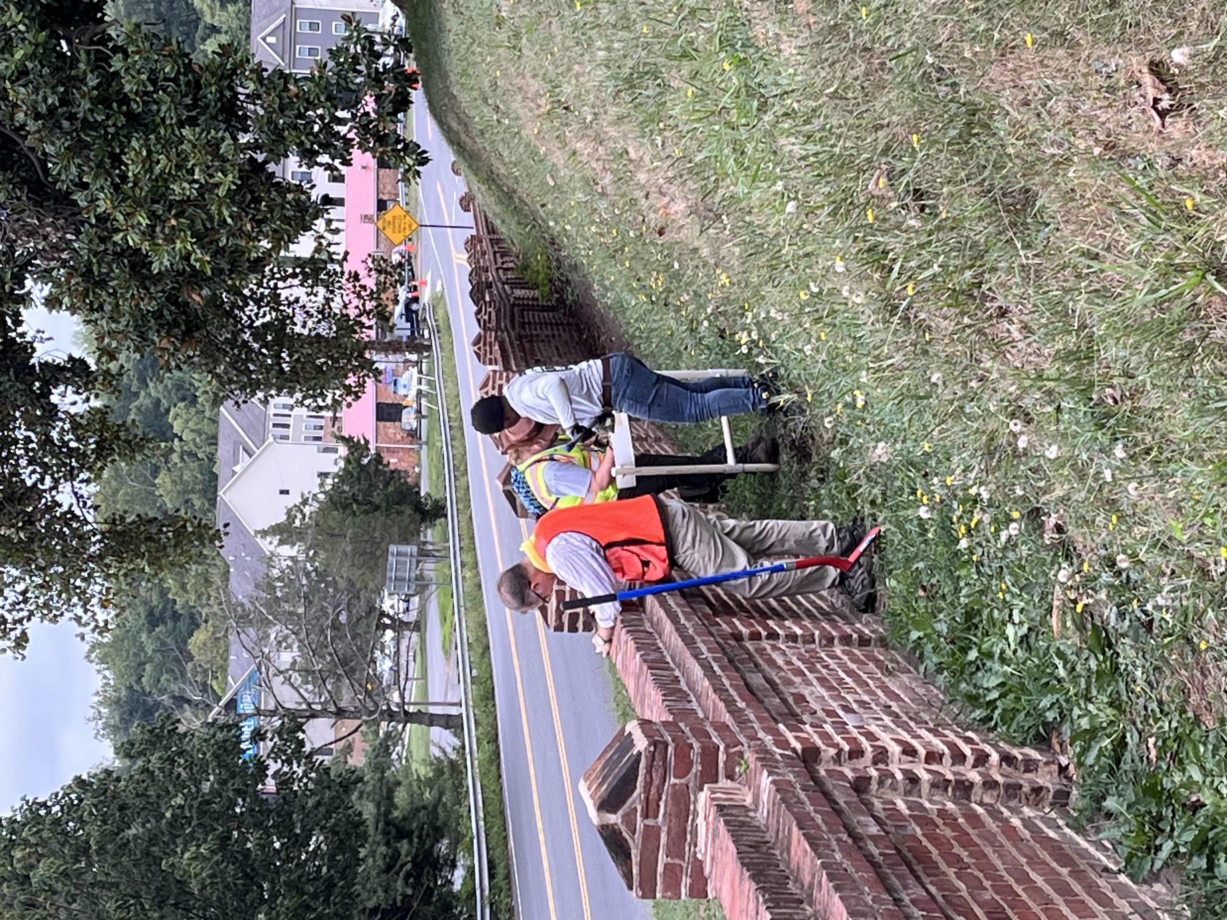 Several NPS employees work alongside a brick wall at the base of a grassy incline that is the Fredericksburg National Cemetery
