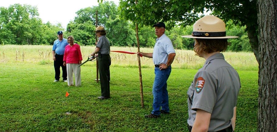 Two park employees and three Friends of Wilderness Battlefield members dedicate new trail by cutting red ribbon with large scissors Two park employees and three Friends of Wilderness Battlefield members dedicate new trail by cutting red ribbon with large scissors