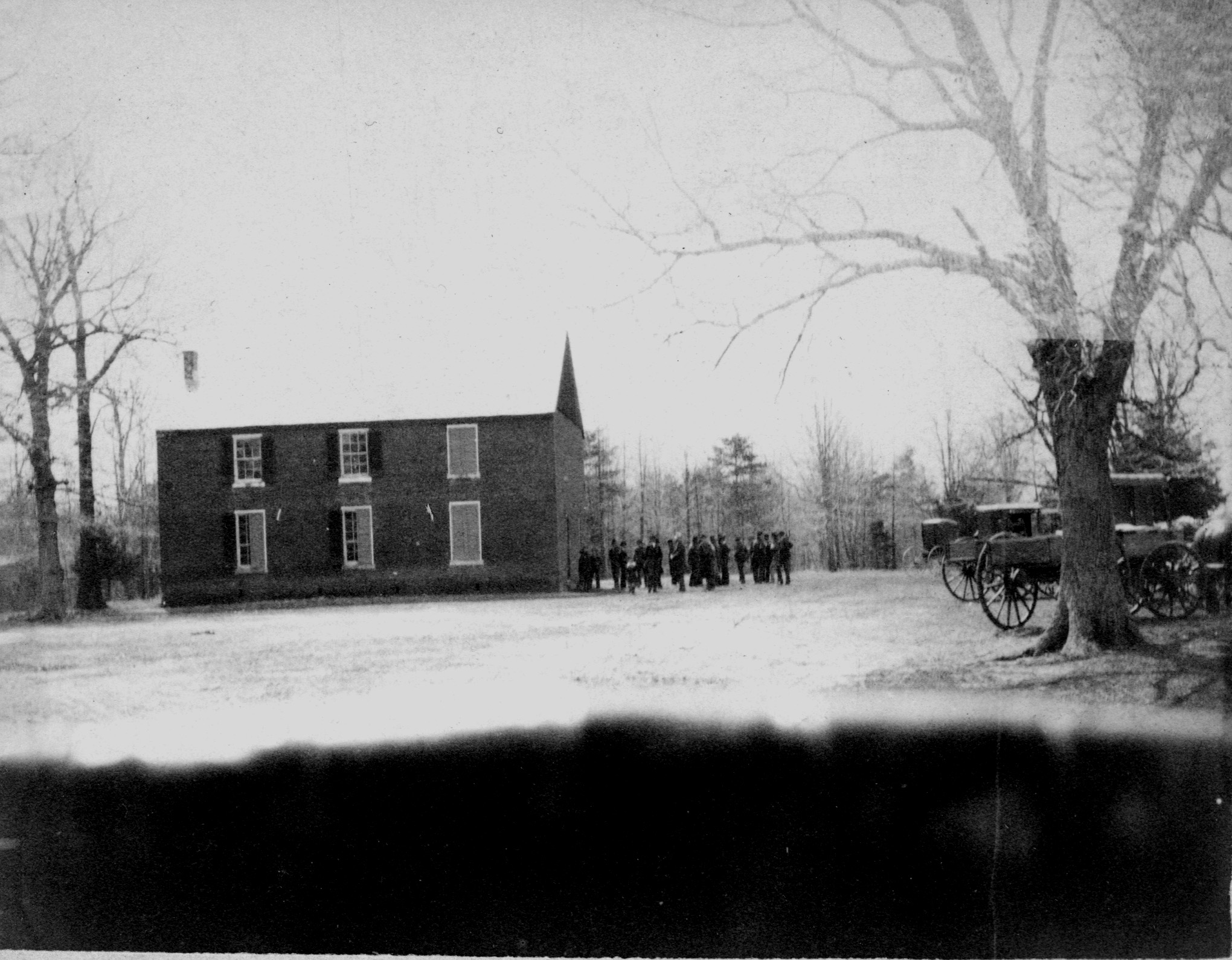 Black and white photo of veterans gathering to the right of a two-story, rectangular, brick building.