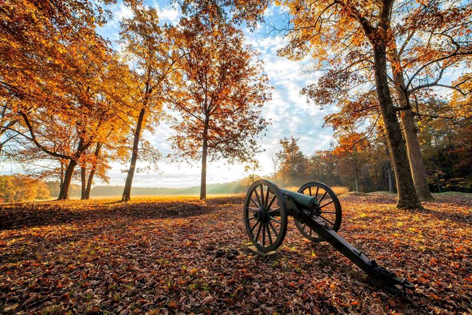 Field with cannon and earthworks covered in orange and golden leaves with trees showing fall colors