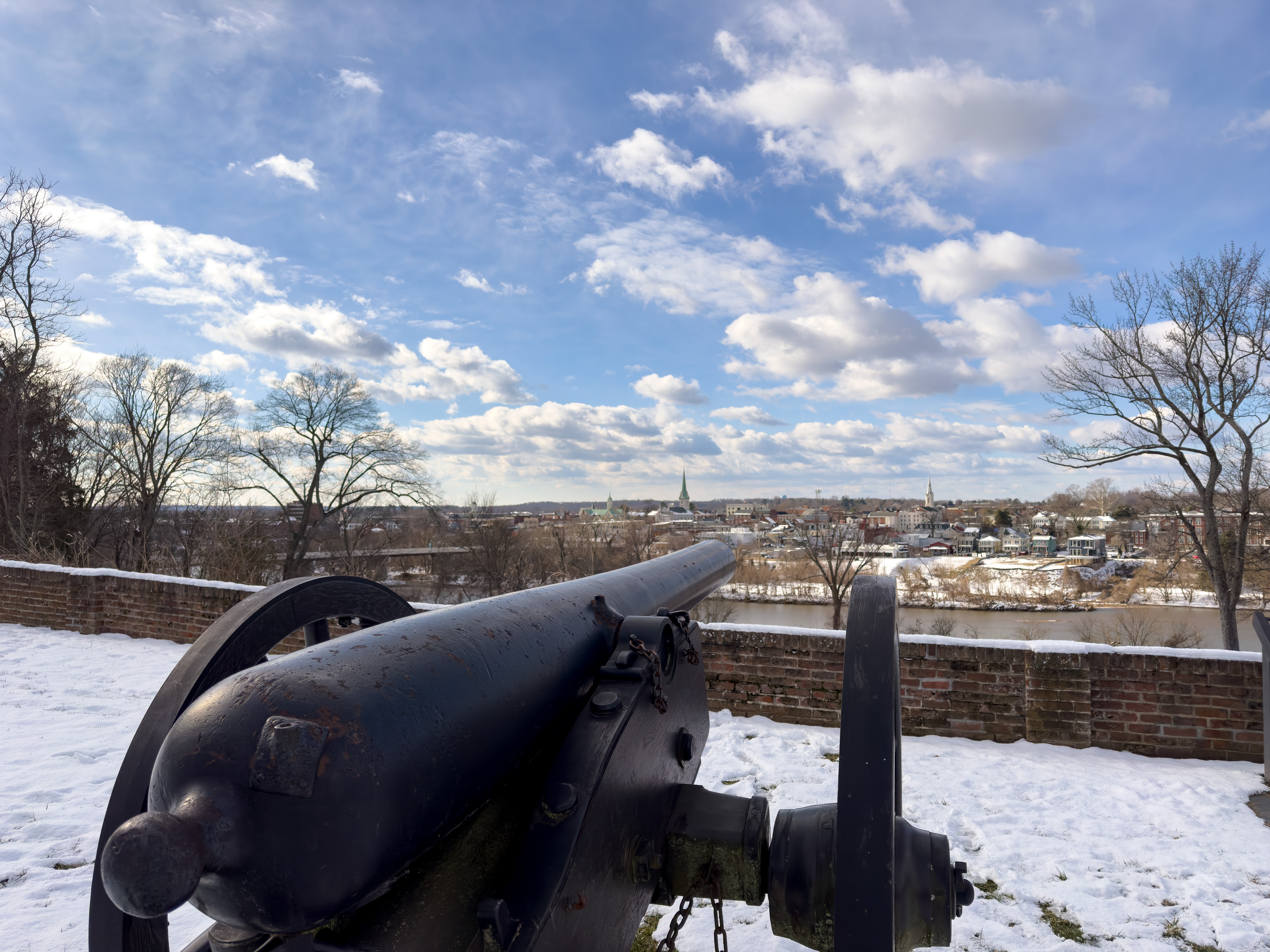 A cannon pointed acorss a river to a town surrounded by snow.