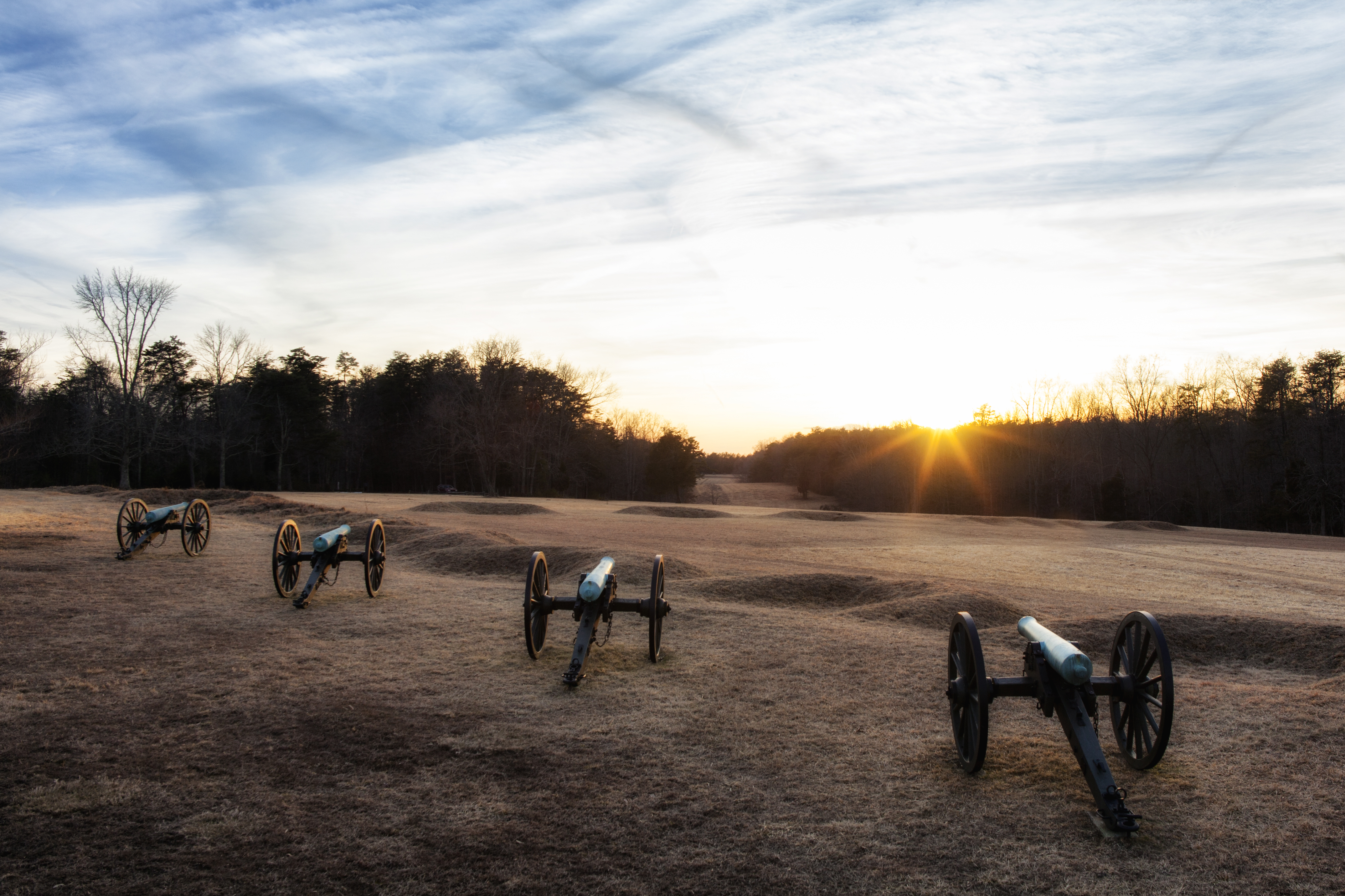 A line of cannons pointed across an open field at sunrise.