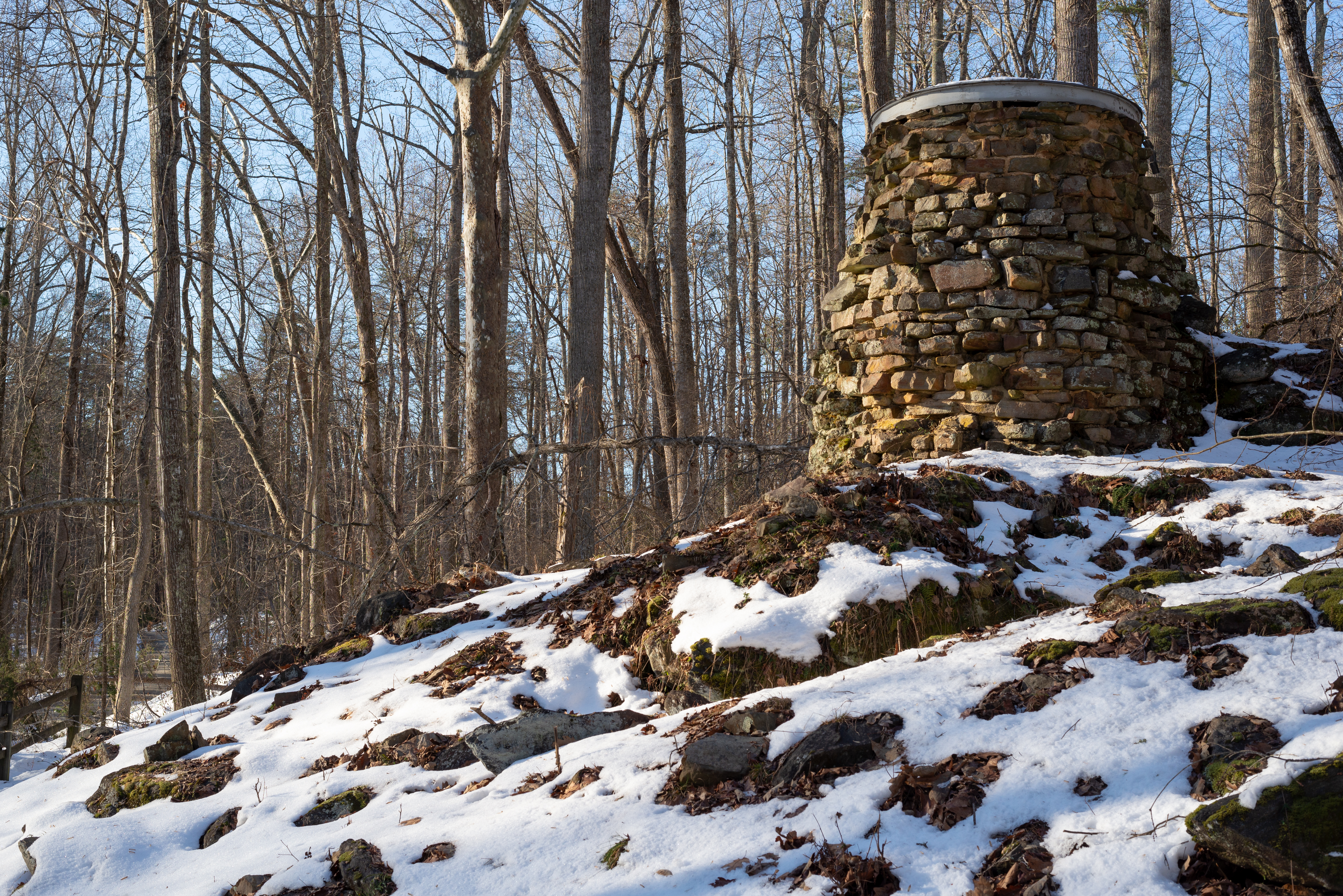 A stone furnace stack on a rocky mound surrounded by a thin layer of snow.