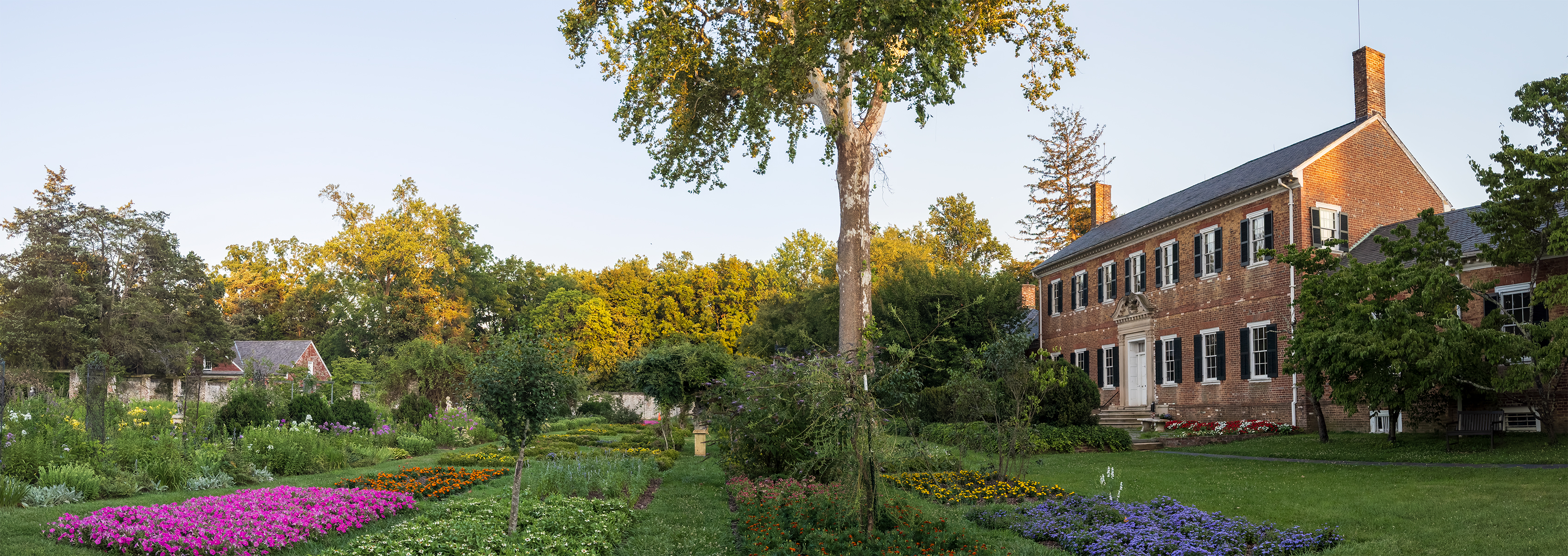 A two story brick Georgian mansion with colorful gardens in front of the house.