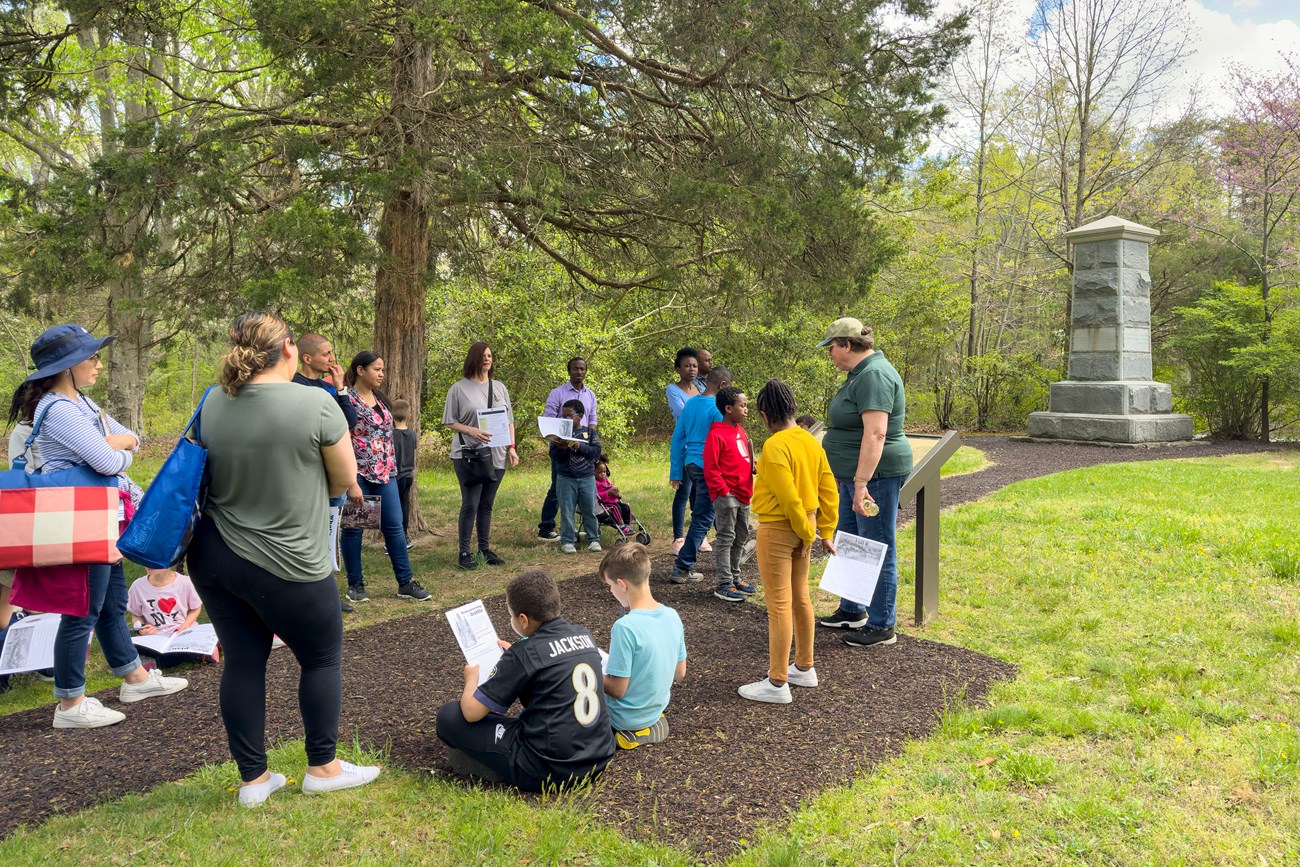 A park volunteer peaks to a group of children and adults.