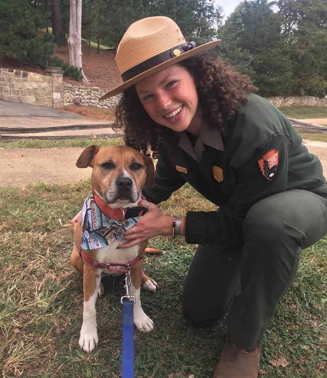 A Park Ranger poses with a dog along a historical dirt road.