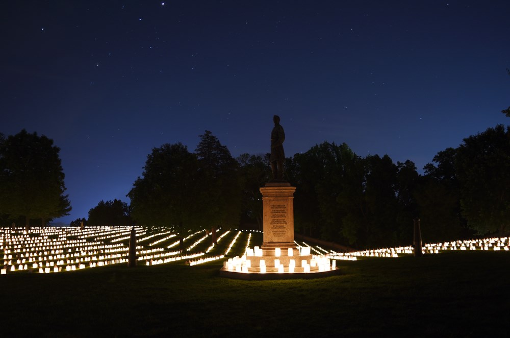 Graves illuminated by candles with large monument in center at night