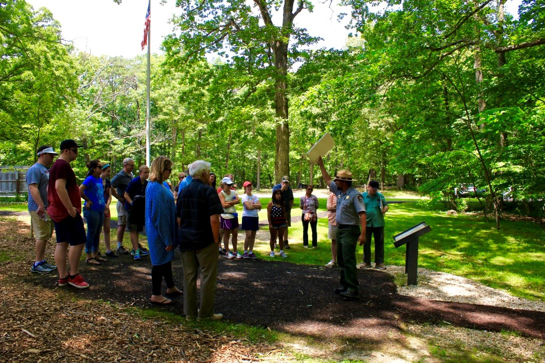 Ranger leads group of visitors on guided walking tour with trees and flag pole in background