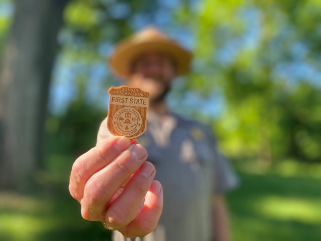 A ranger holds up a Junior Ranger badge.