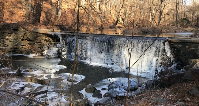 Icy, cold stream water flowing over a small dam, crashing onto rocks.